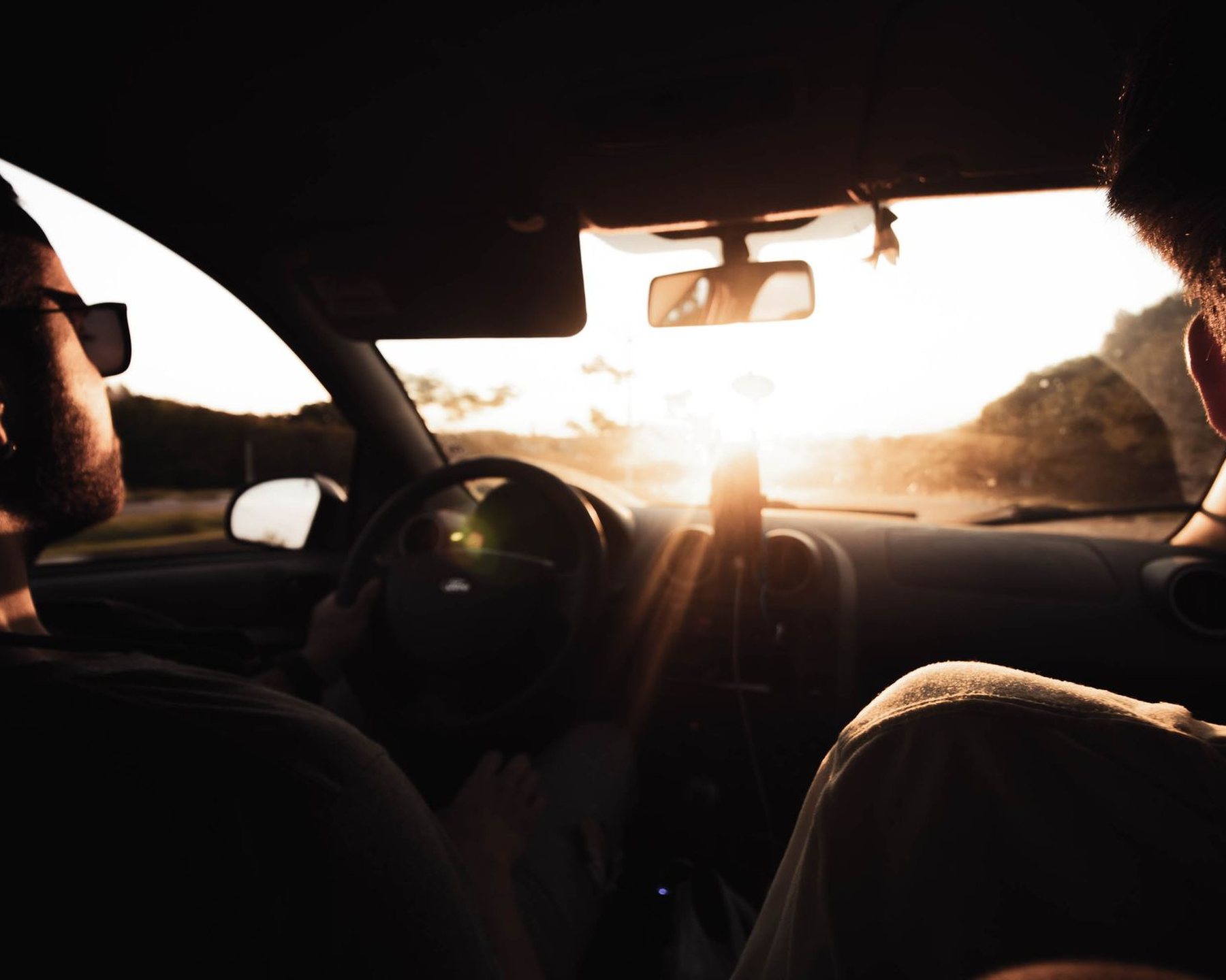 Two people in a car with the sun low ahead of them