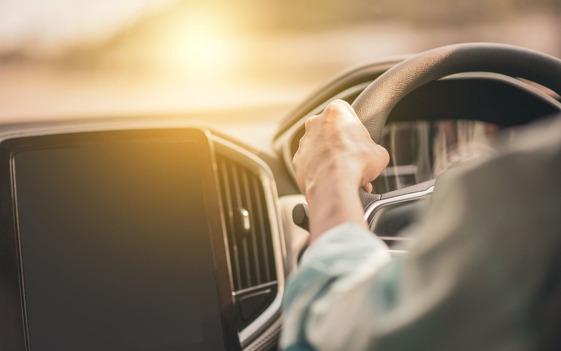 A hand on the steering wheel with sunlight through the windscreen
