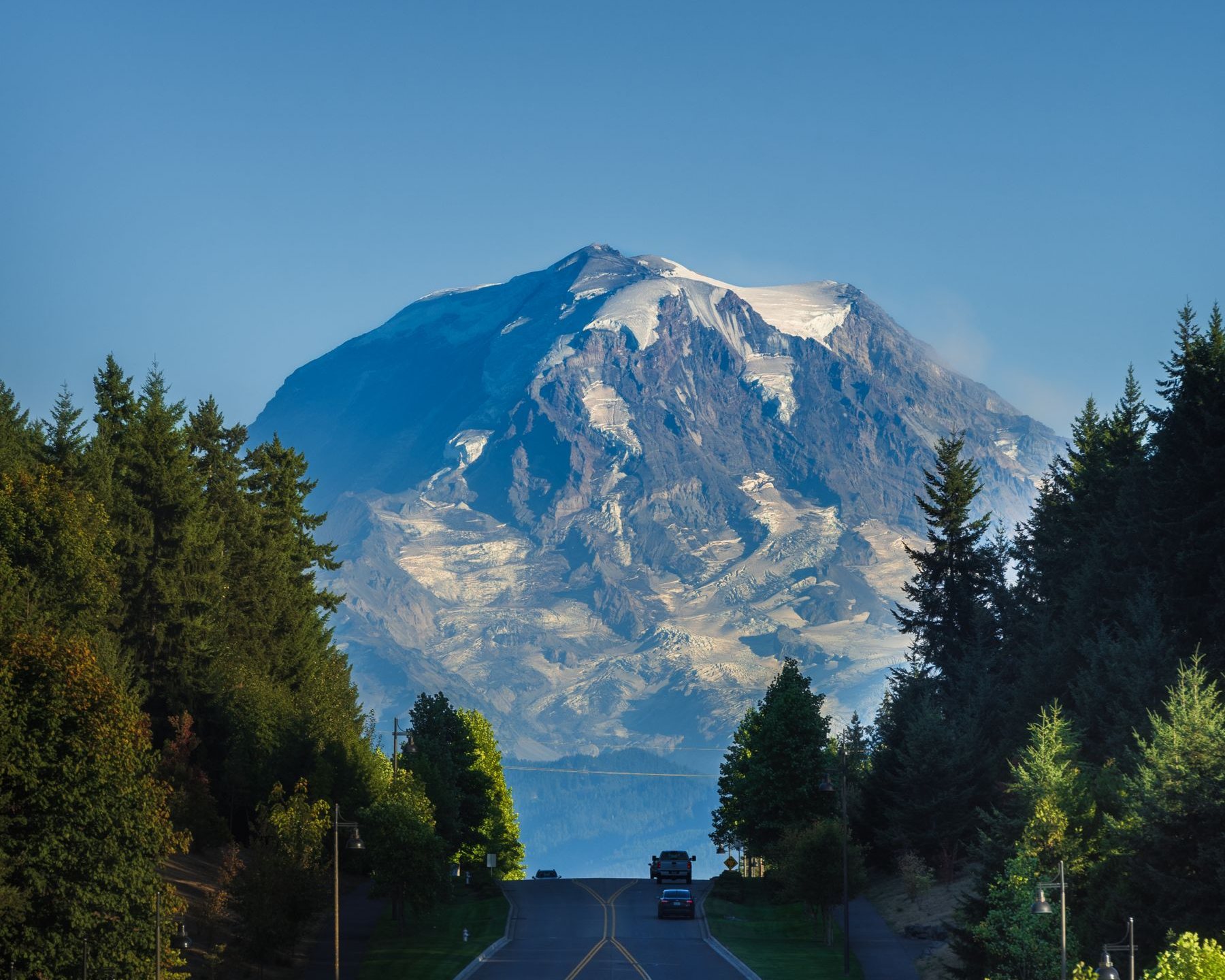 A road running through forest towards a snow capped mountain